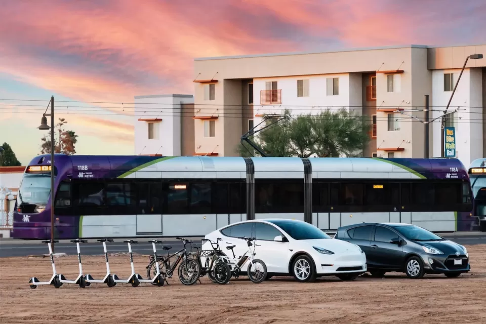 Rendering of electric scooters, electric cars, light rail train, and apartments in background.